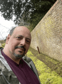 a man standing in front of a brick wall with moss growing on it