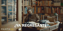 a man sits at a desk in front of a bookshelf with the words " ya regresaste " on the bottom