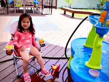 a little girl in a pink bathing suit sits in a high chair on a deck