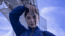 a woman wearing a blue sweater holds her hand to her forehead