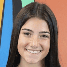 a close up of a young woman 's face smiling in front of a colorful wall .