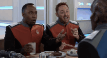 two men are sitting at a table with plates of food and chopsticks