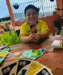 a young boy is sitting at a table playing a game of uno cards .