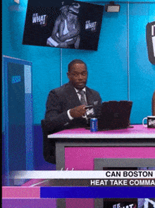 a man in a suit and tie is sitting at a desk with a laptop and a can of soda