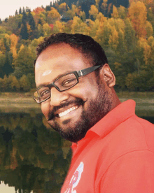 a man wearing glasses and a red shirt with the letter p on it smiles