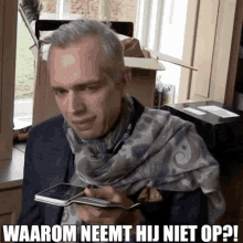 a man with a scarf around his neck is holding a cell phone and says waarom neemt hij niet op