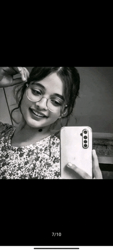 a girl wearing glasses is taking a selfie with her cell phone .