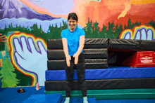 a woman in a blue shirt stands in front of a wall with a painting of a hand