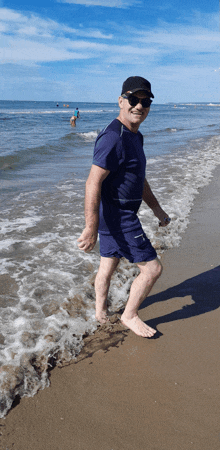 a man in a blue shirt and shorts stands on the beach