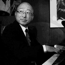 a man in a suit and tie is playing a piano in a black and white photo .