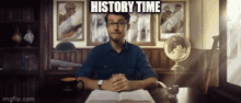 a man is sitting at a desk with a book and a sign that says " history time " above him