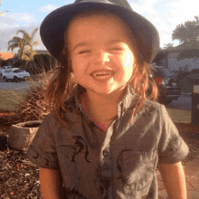 a little girl wearing a hat and a shirt with dinosaurs on it smiles