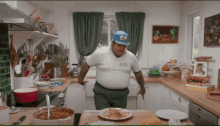 a man standing in a kitchen with a plate of food on the counter and a hat that says ' california ' on it