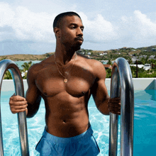 a shirtless man in blue shorts is holding onto a metal railing in a pool