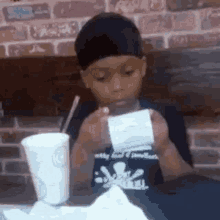 a young boy is sitting at a table holding a receipt and a cup of soda .