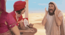 a man with a beard and a turban is talking to a woman in a pink dress and a man in a white robe