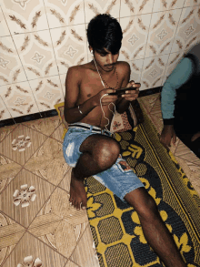 a shirtless man is sitting on a rug looking at his cell phone