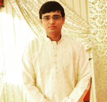 a young man wearing glasses and a white shirt stands in front of a curtain