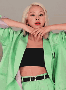 a woman with blonde hair is wearing a green jacket and a black crop top .