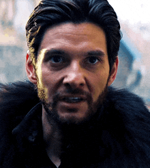 a close up of a man 's face with a beard wearing a fur coat .