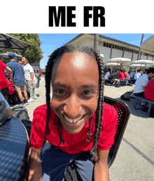 a young man in a red shirt is smiling in front of a sign that says " me fr "