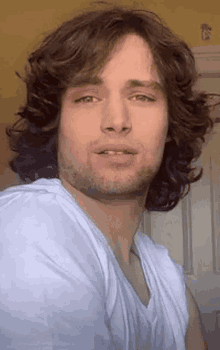 a man with long curly hair and a beard is wearing a white shirt .