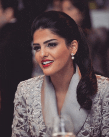 a woman wearing pearl earrings and a grey jacket smiles for the camera