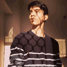 a young man wearing a striped sweater is standing in front of a window