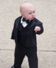 a baby in a tuxedo and bow tie is pointing at the camera .