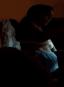 a woman is sitting on a couch in a dark room with her shirt off .