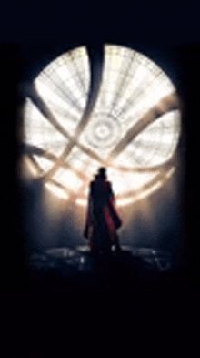 a man in a red coat is standing in front of a large window with a light coming through it .