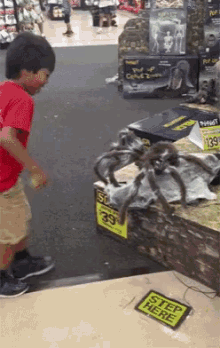 a boy is standing in front of a giant spider in a store with a sign that says " step here "