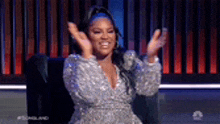 a woman in a silver dress is sitting in a chair and clapping her hands .