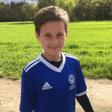 a young boy wearing an adidas shirt stands in a grassy field