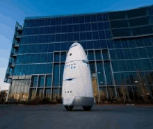 a white robot is standing in front of a large building .