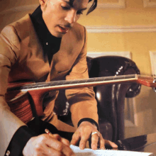 a man in a tan suit is writing on a piece of paper while playing a guitar