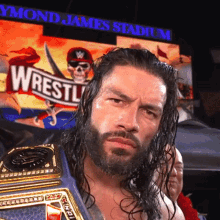 a man with a beard is holding a wrestle belt in front of a sign that says raymond james stadium