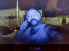 a man with a mustache is talking on a cell phone in front of an exctel sign