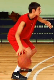 a young man in a red shirt is dribbling a basketball on a court .