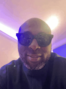 a bald man wearing sunglasses and a black shirt smiles