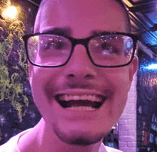 a man wearing glasses and a beard is smiling in a bar .