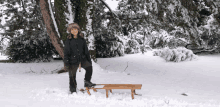 a young boy stands next to a wooden sled in the snow