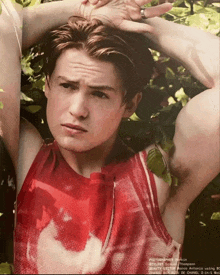 a young man in a red tank top is standing in a forest