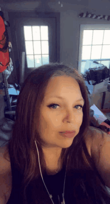 a woman wearing headphones takes a selfie in front of a window in a messy room