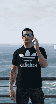 a man wearing a black adidas t-shirt stands in front of a body of water