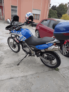 a blue dakar motorcycle is parked in front of a red car