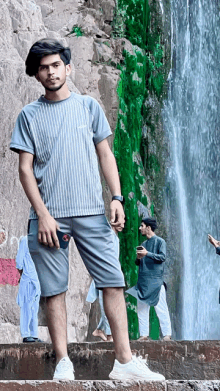 a young man standing in front of a waterfall wearing a nike shirt