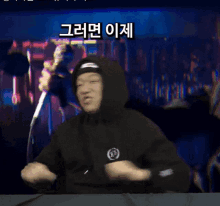 a man wearing a black hoodie is dancing in front of a microphone with korean writing behind him