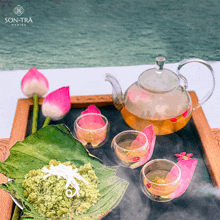 a glass teapot sits on a wooden tray next to a bowl of green rice and a cup of tea