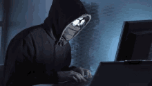 a man in a hoodie and glasses is typing on a laptop .